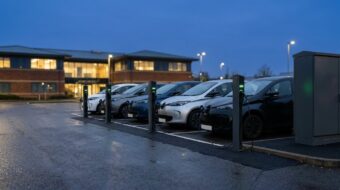 Electric cars charging from AC pedestals at a workplace car park, with the electrical cabinet that supplies them
